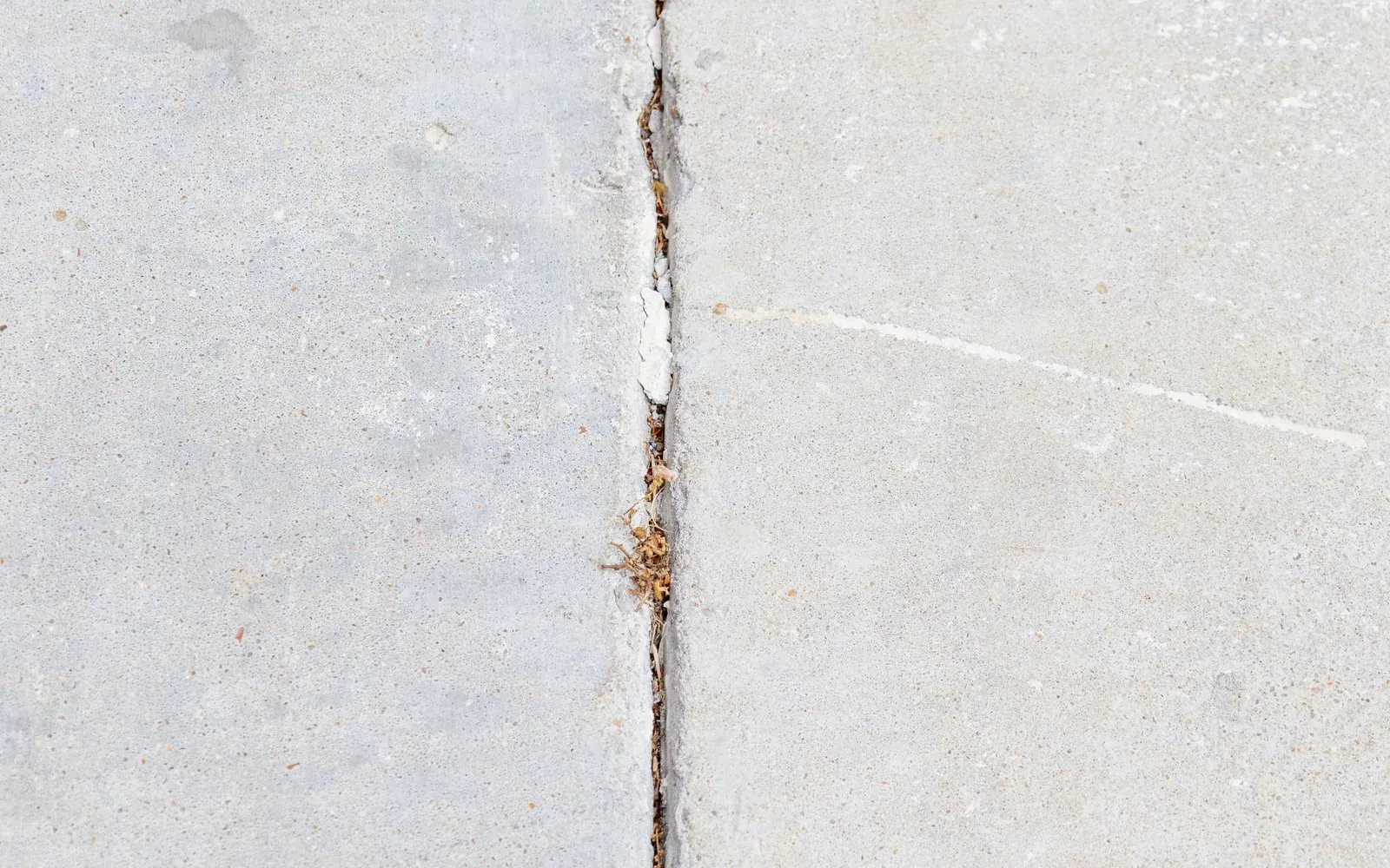 Open joint in a concrete floor with crumbling edges and debris packed into the gap