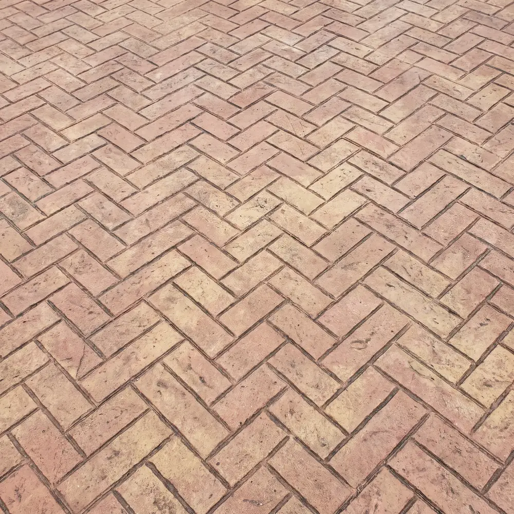 Herringbone brick stamp pattern pressed into a concrete slab in muted red