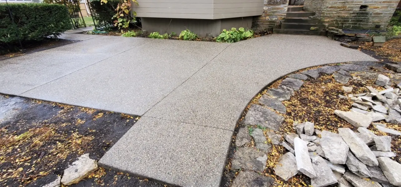 Exposed aggregate walkway and landing wrapping a home with a dark trowel finished border